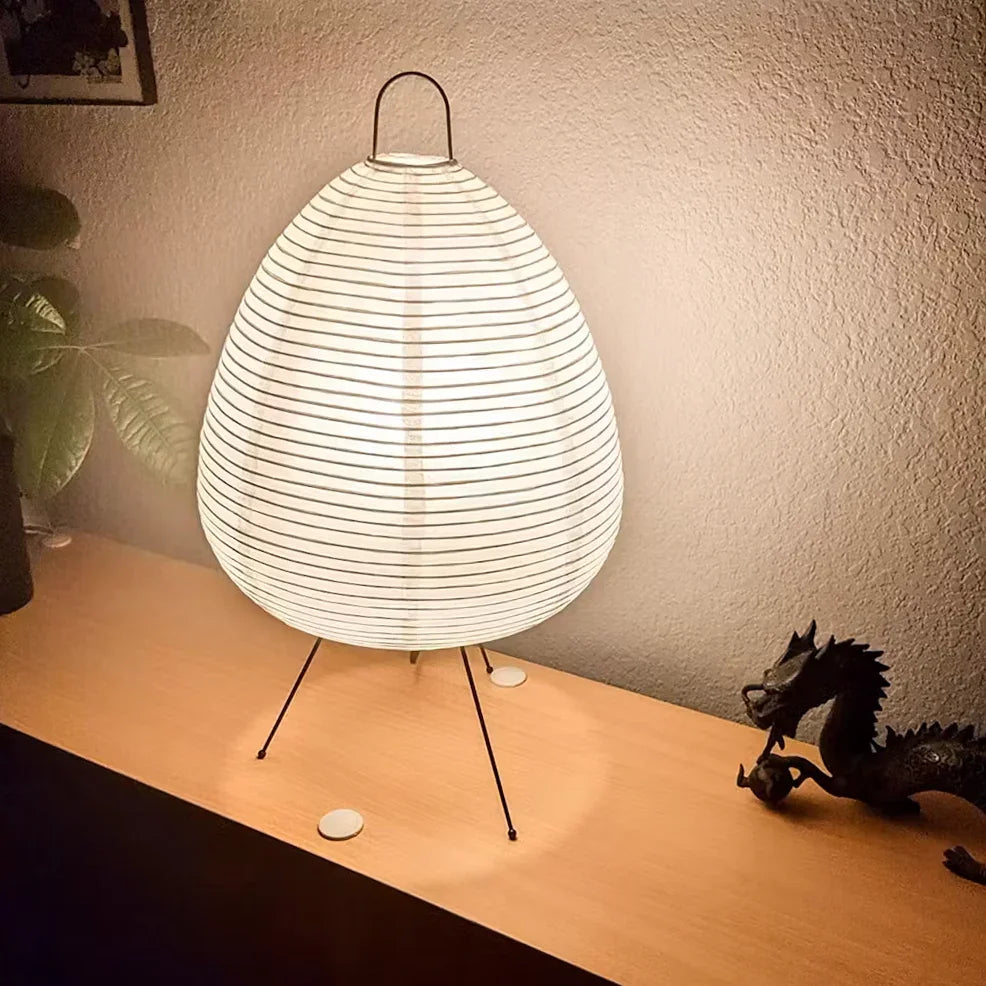 A Hachi Paper Lamp glowing on a wooden sideboard beside a small dragon figurine