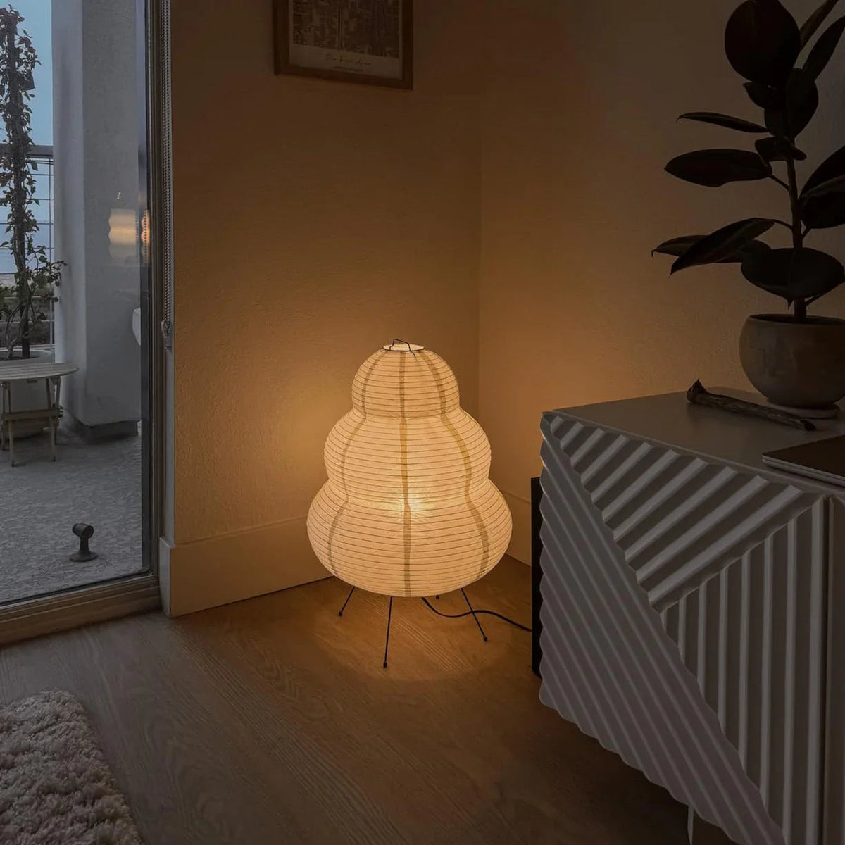 A Keichi Paper Lamp glowing on the floor in the corner of a living room