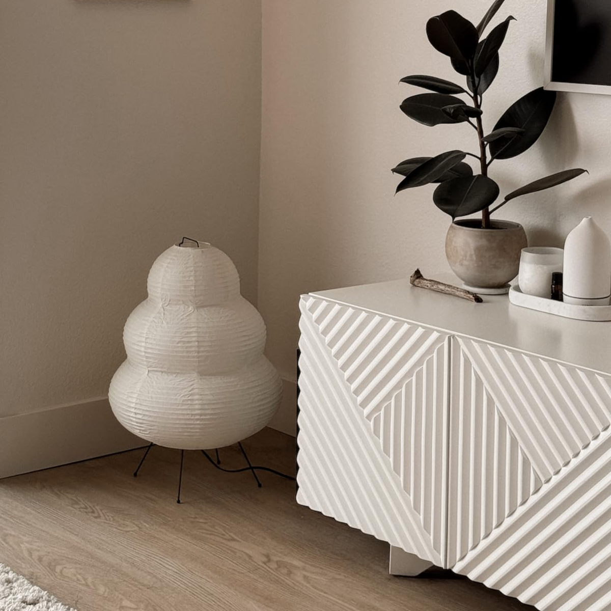 A Keichi Paper Lamp standing on the floor beside a white sideboard and a potted plant