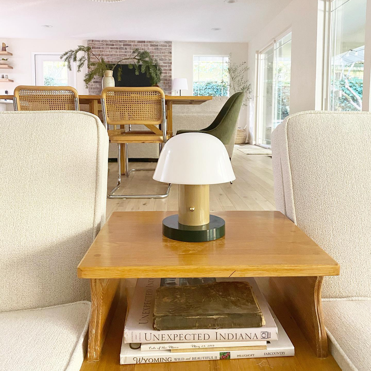 A Lecce Portable Lamp on a wooden side table between two armchairs in a bright living room