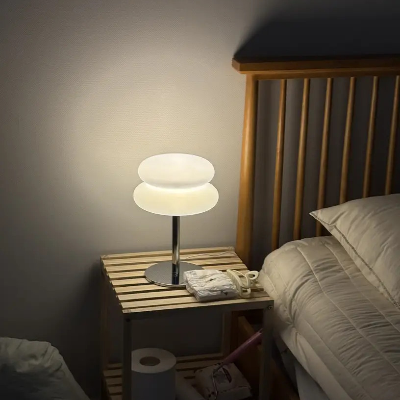 An Opal White Verdon Table Lamp glowing on a bedside table next to a bed