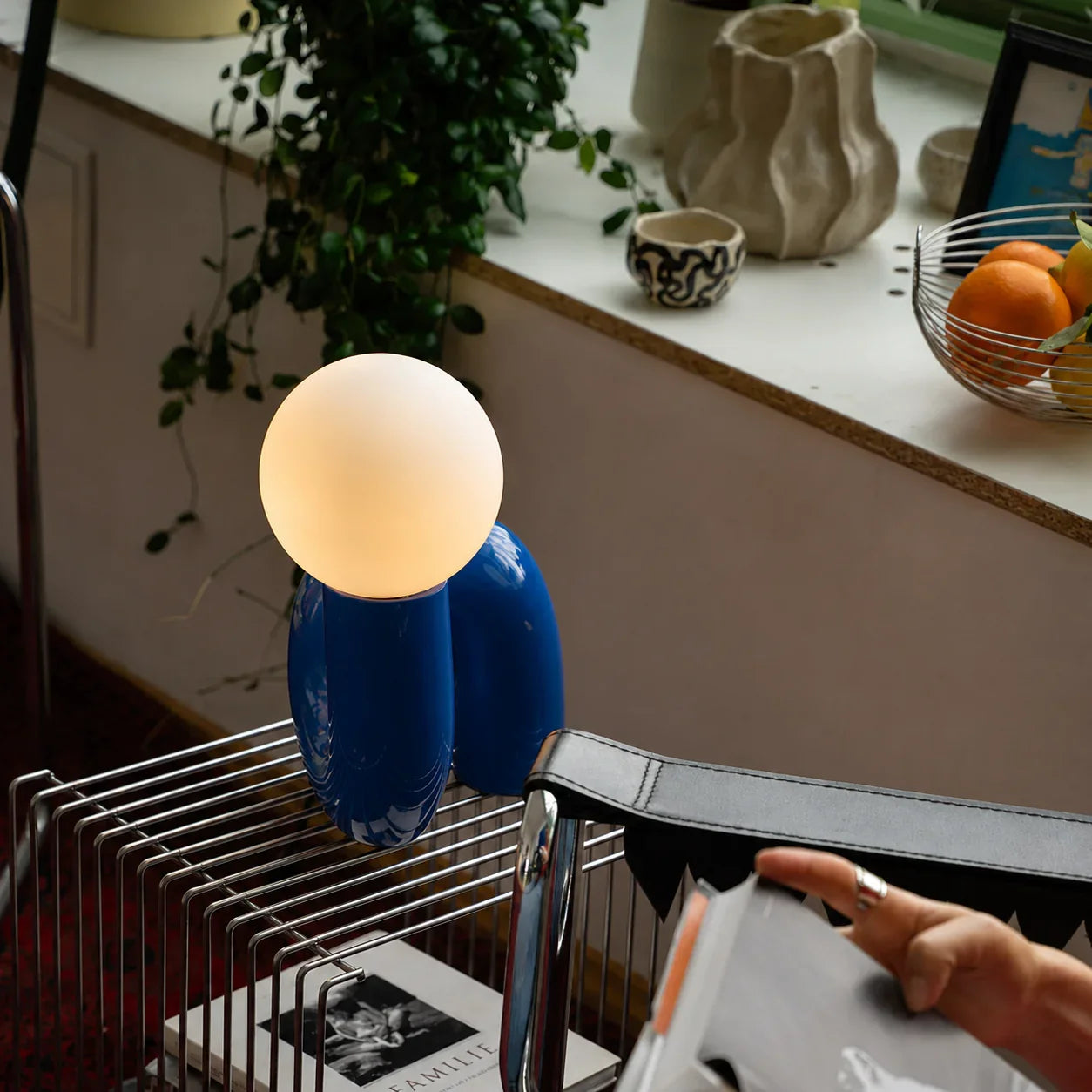 Blue groovy table lamp with glowing orb, styled on a wire shelf with plants and decor