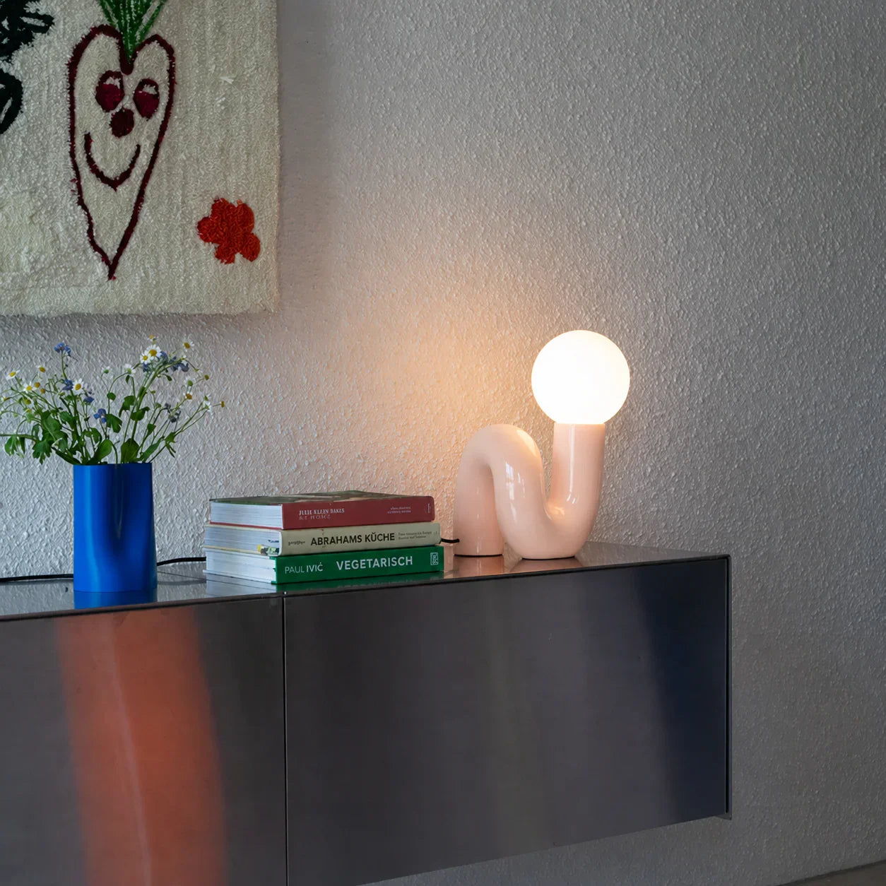 Groovy pink lamp with curved design on modern console, styled with books and flowers