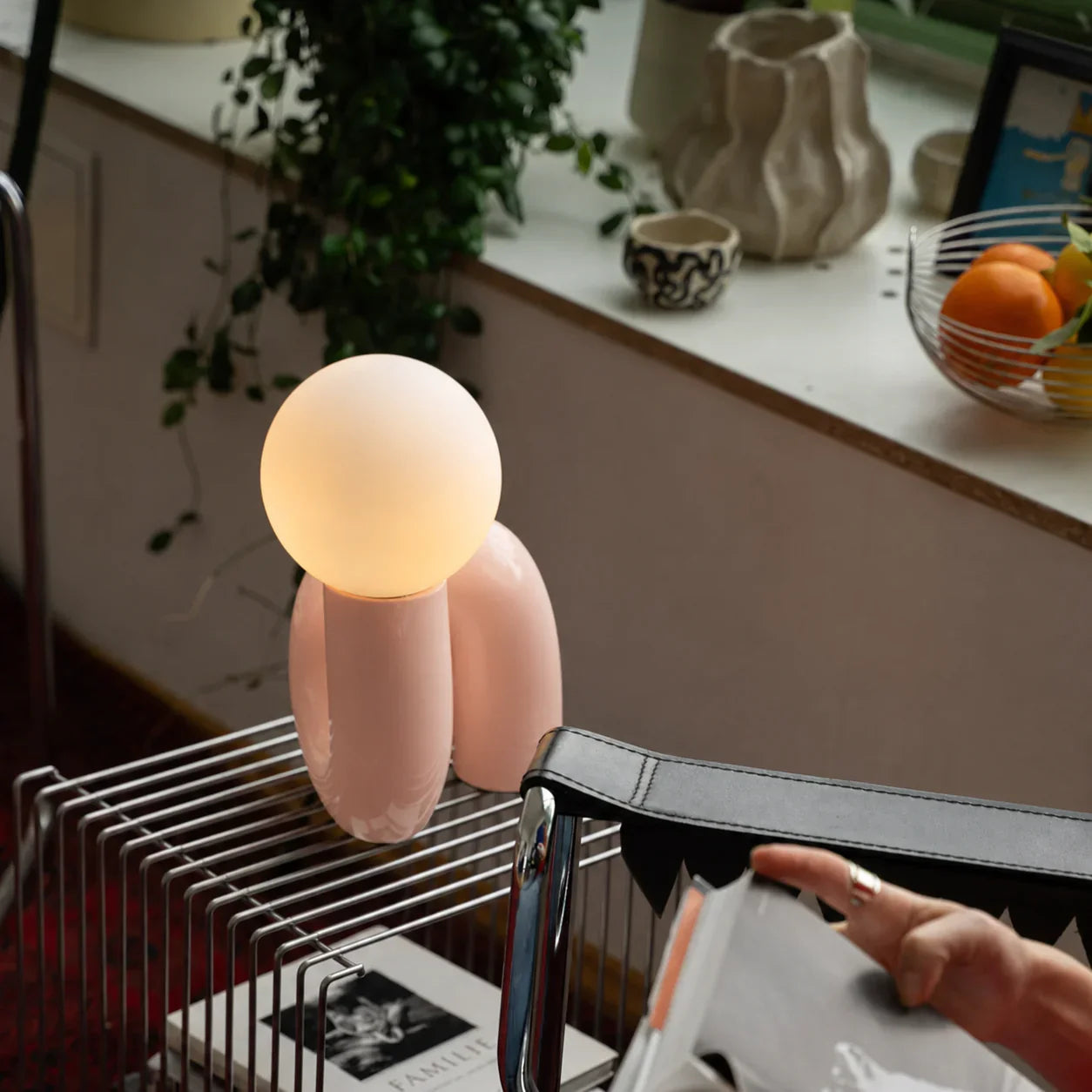 Pink modern lamp with glowing orb, styled on metal cart beside plants and decor