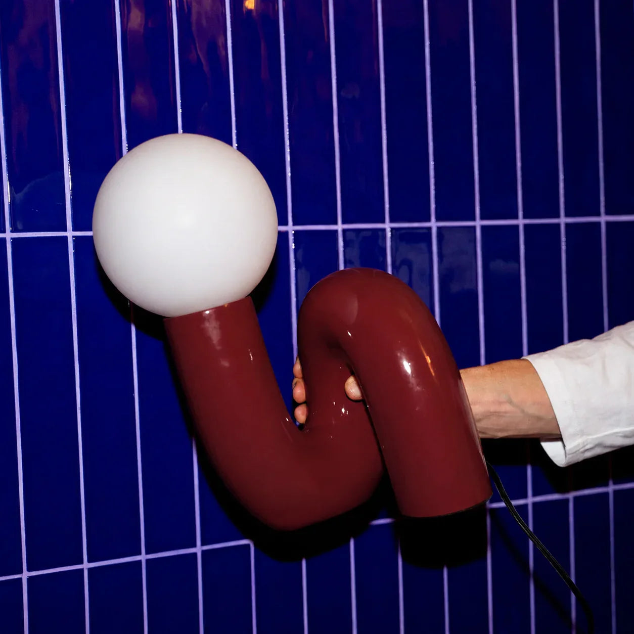 Groovy red curved lamp with white globe against blue tiled wall