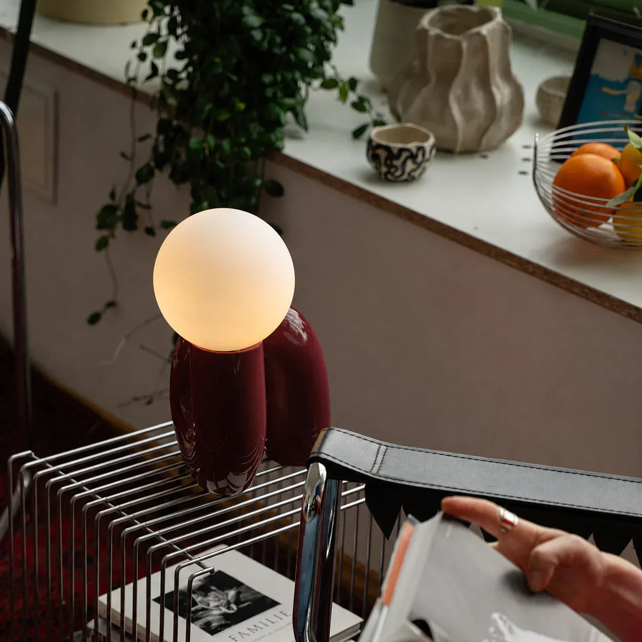 Groovy red table lamp with glowing orb, styled on a metal cart beside plants and decor