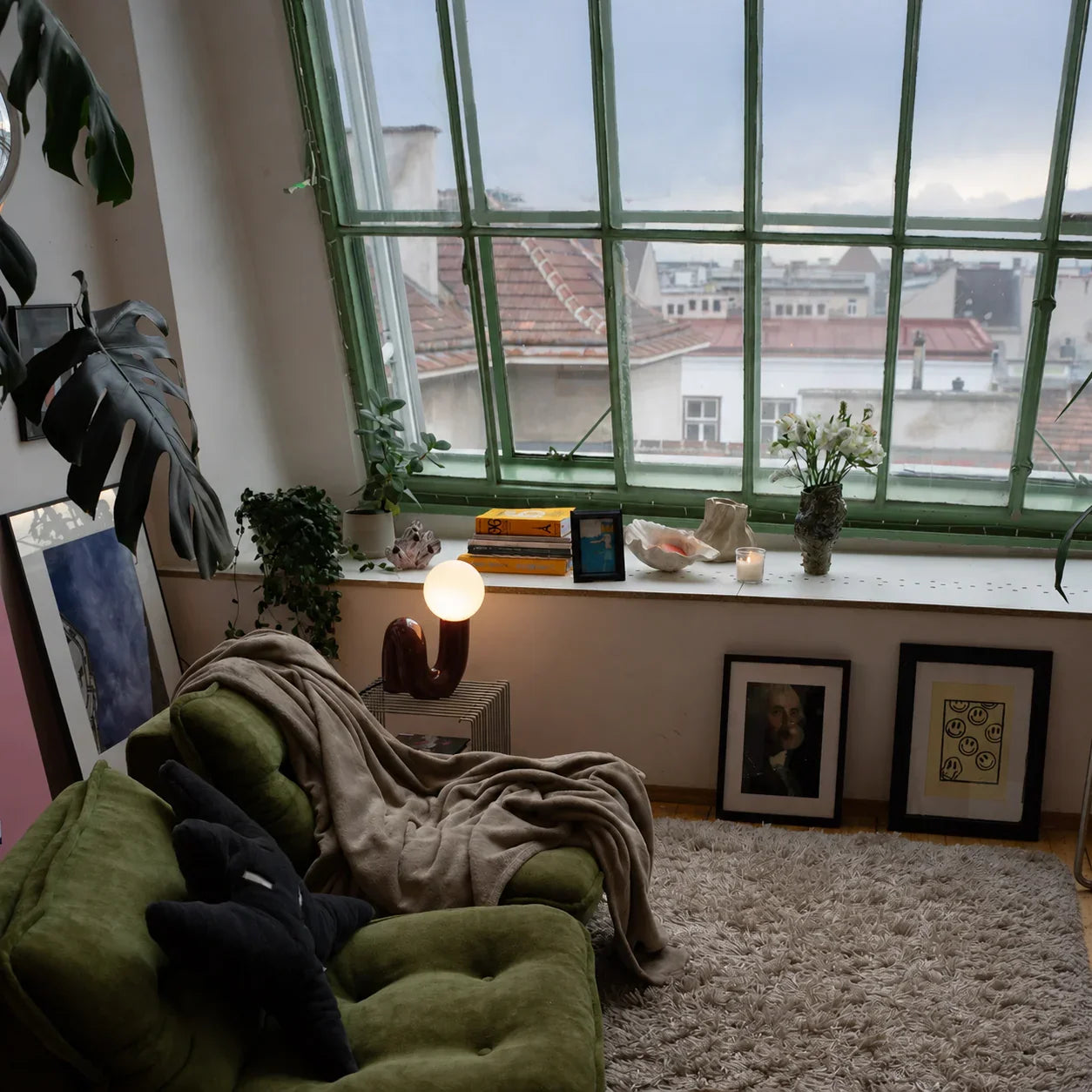 Cozy green armchair with funky lamp, plants, and city view through large window