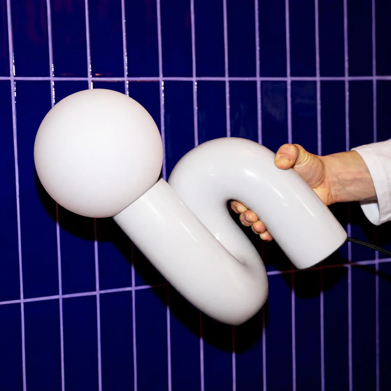 White groovy lamp with curved design held against blue tiled wall