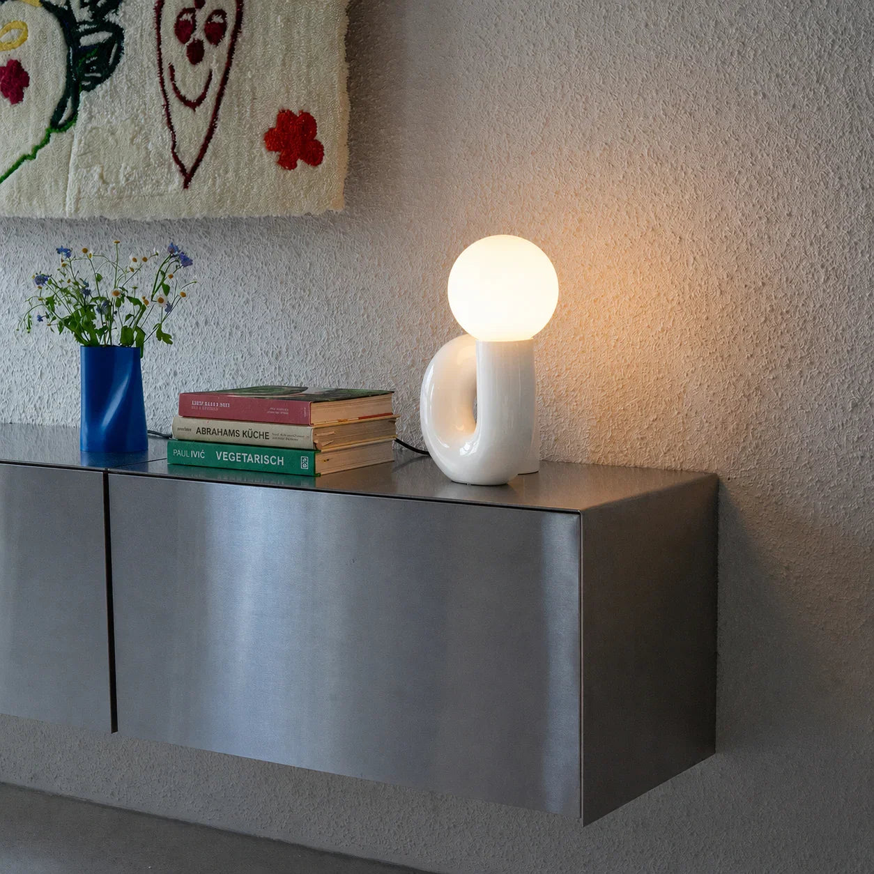 Modern white table lamp with globe bulb on sleek metal console, styled with books and vase for cozy ambiance