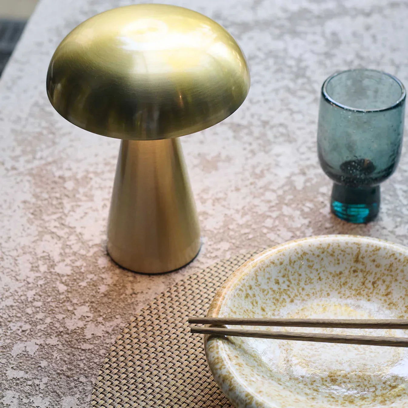 Golden mushroom-shaped lamp on textured table with ceramic bowl and blue glass