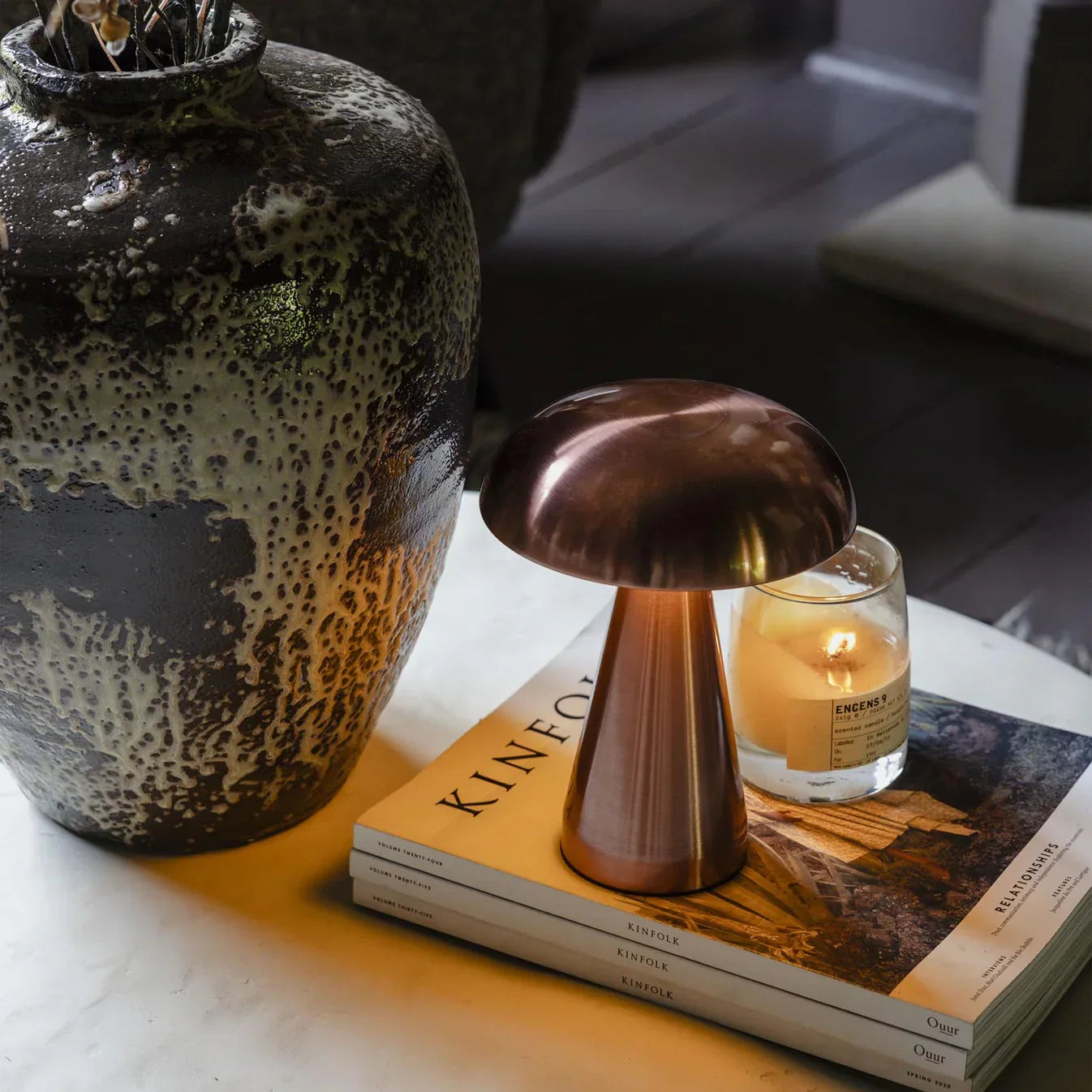 Copper mushroom lamp on Kinfolk magazines beside speckled vase and candle