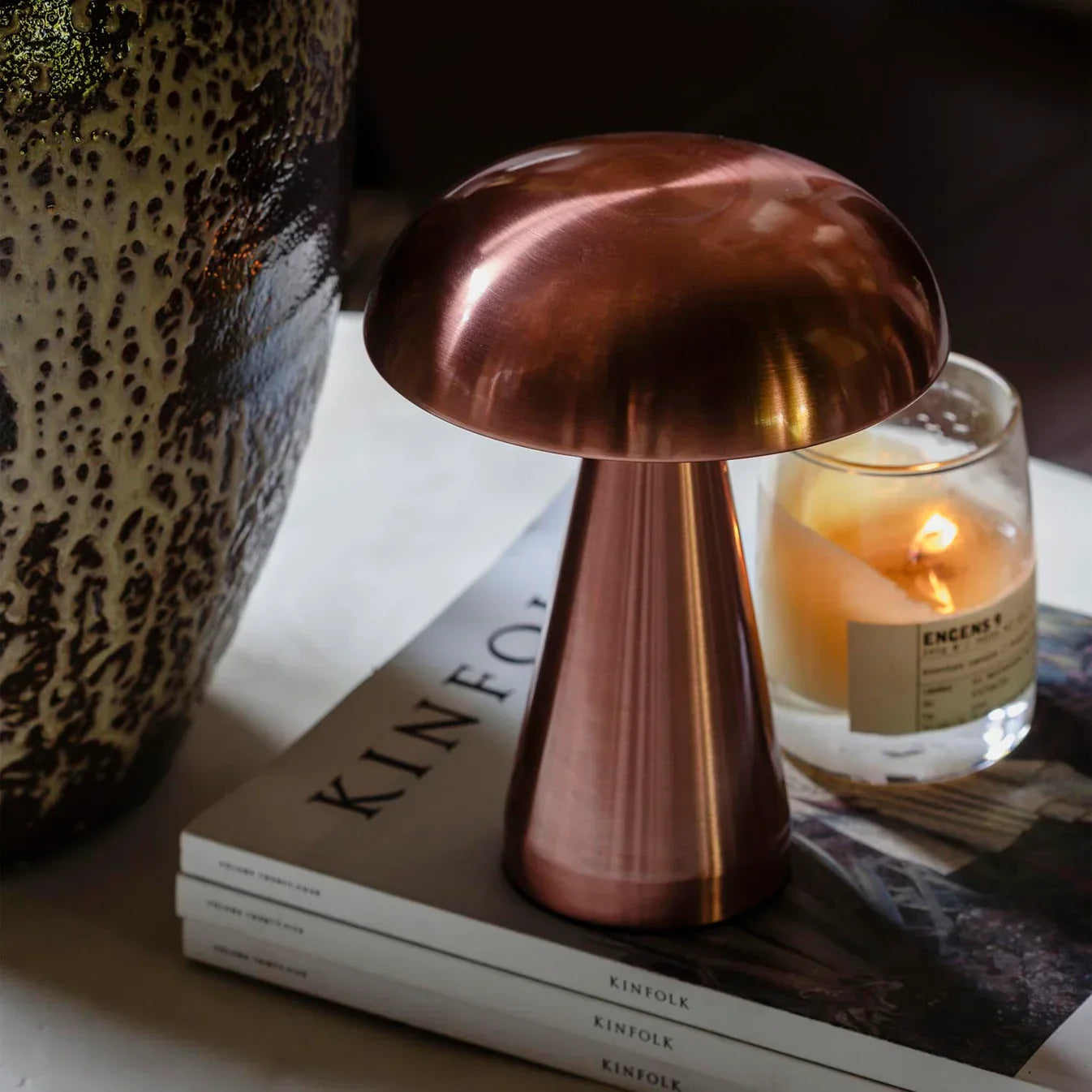 Copper mushroom lamp on Kinfolk magazines beside a lit candle, adding cozy ambiance to home decor.
