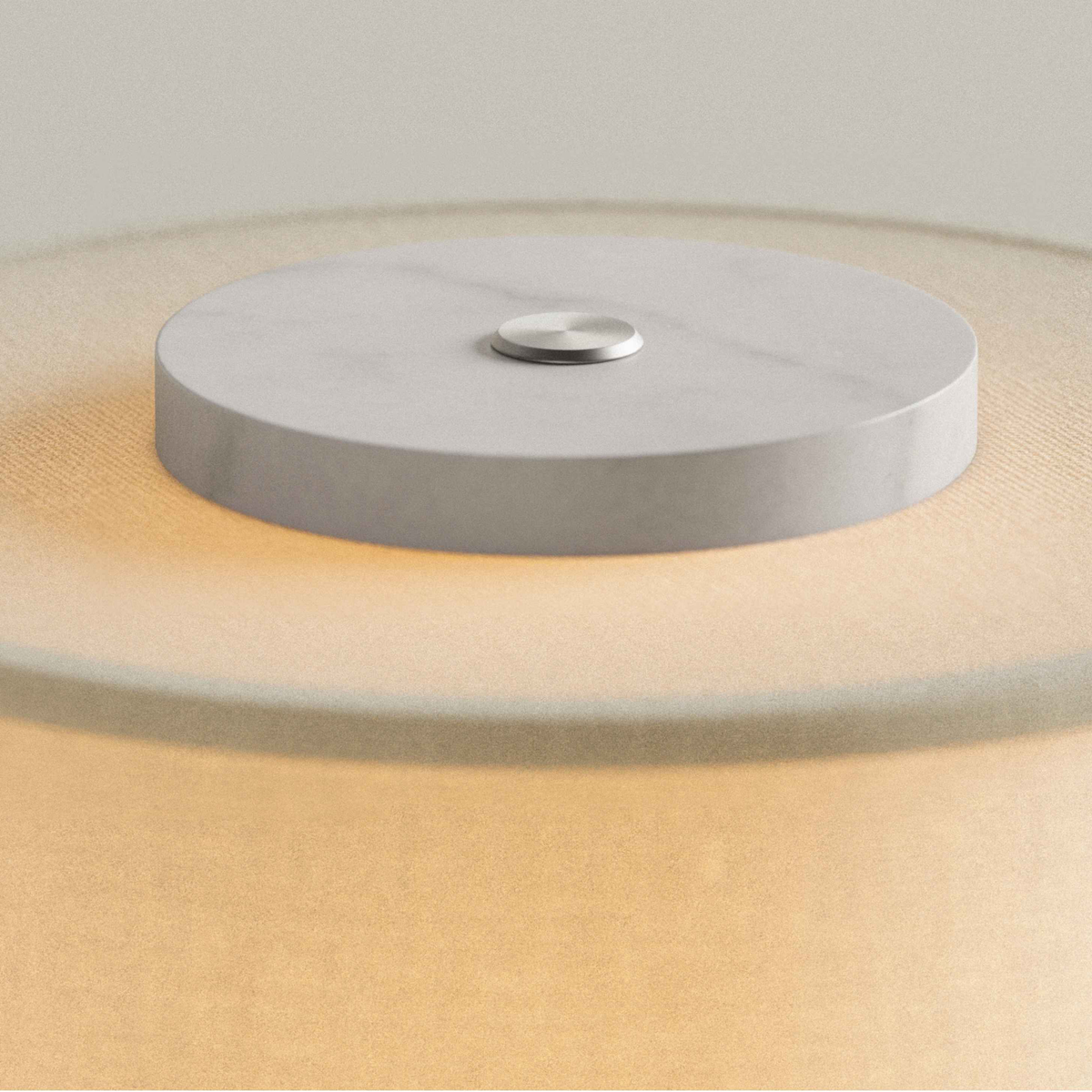 White marble cap with touch button on top of the Olbia Portable Lamp's glowing drum shade