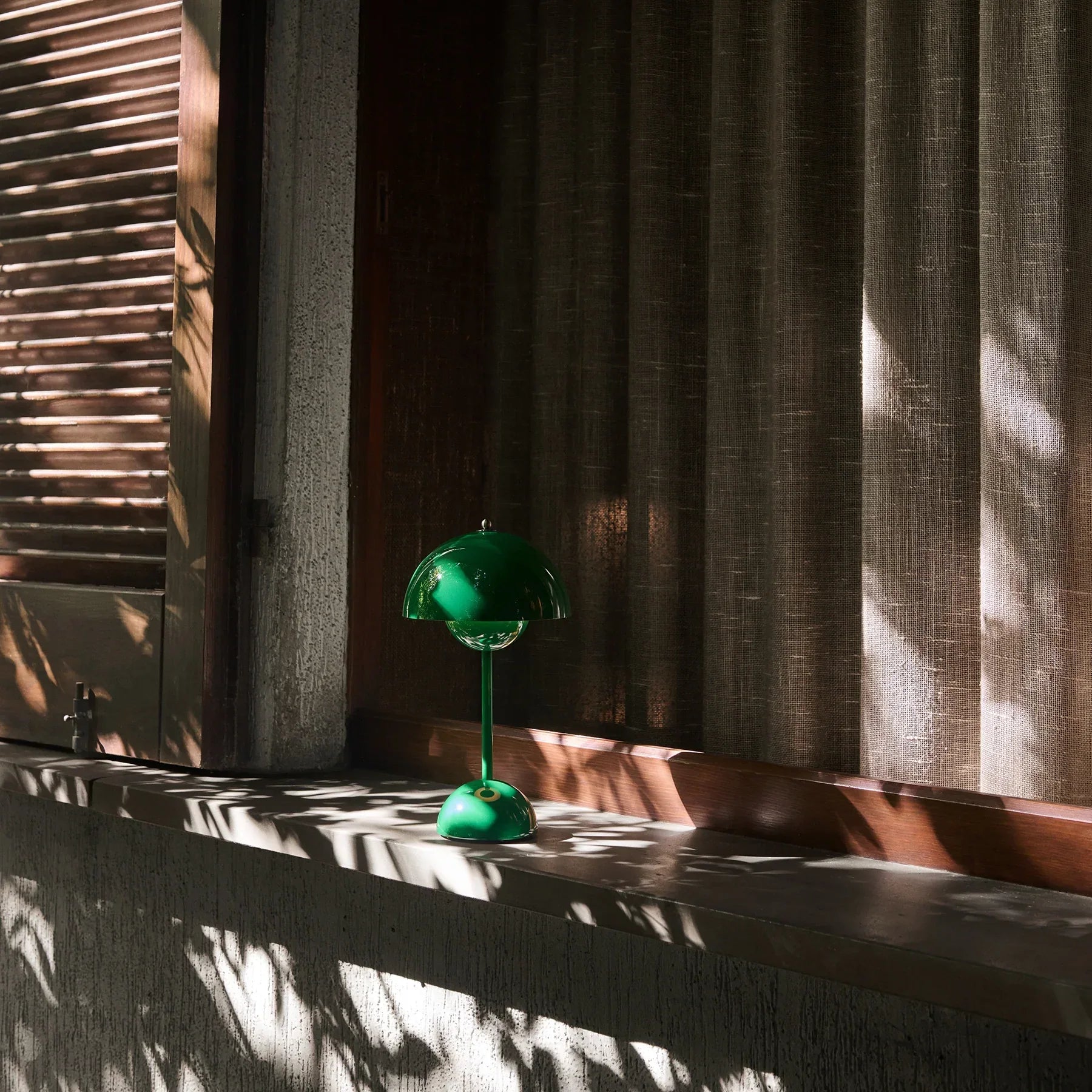 Emerald green dome table lamp on sunlit windowsill, casting leaf shadows, perfect for groovy home decor.