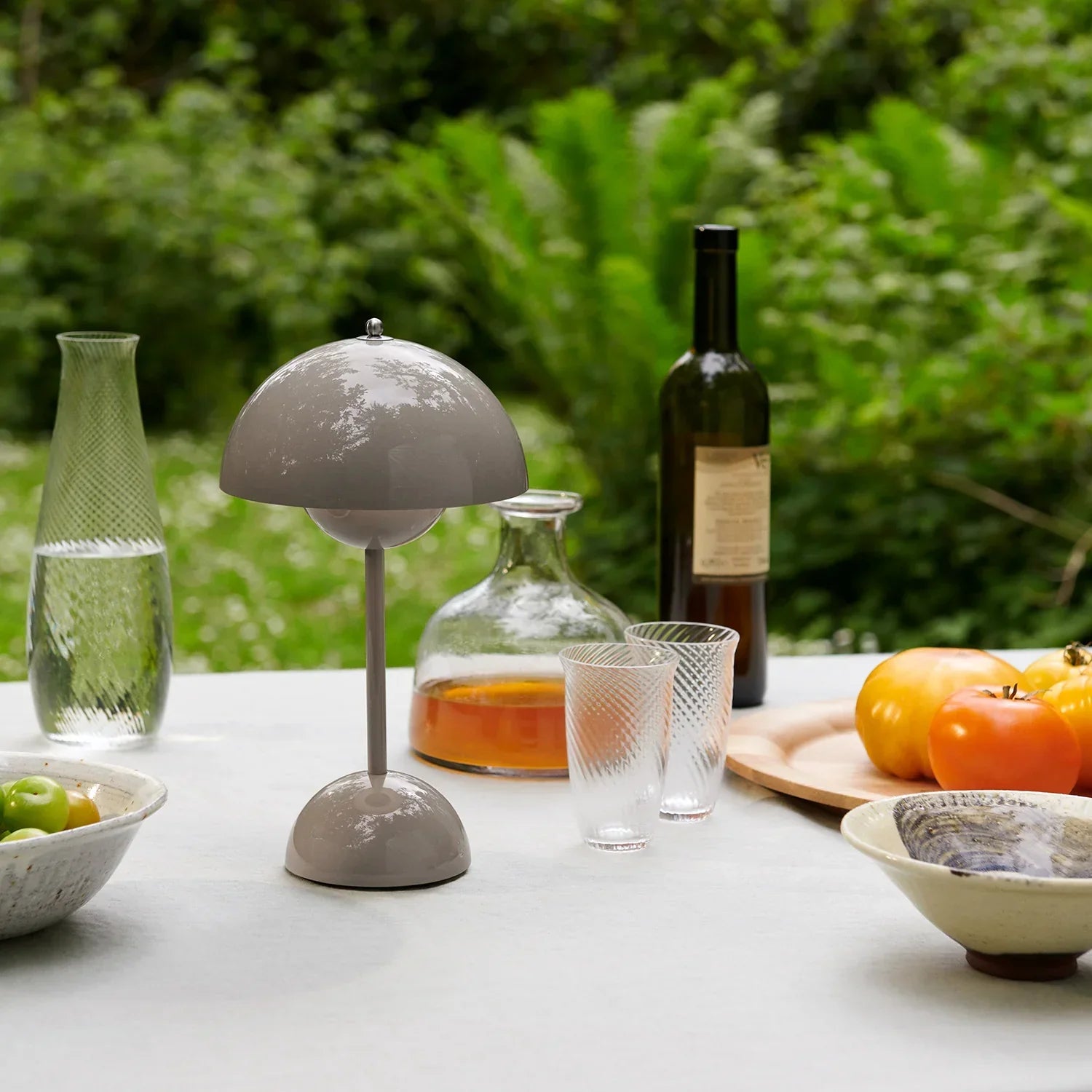 Grey dome table lamp on outdoor dining table with wine, glasses, and fresh tomatoes