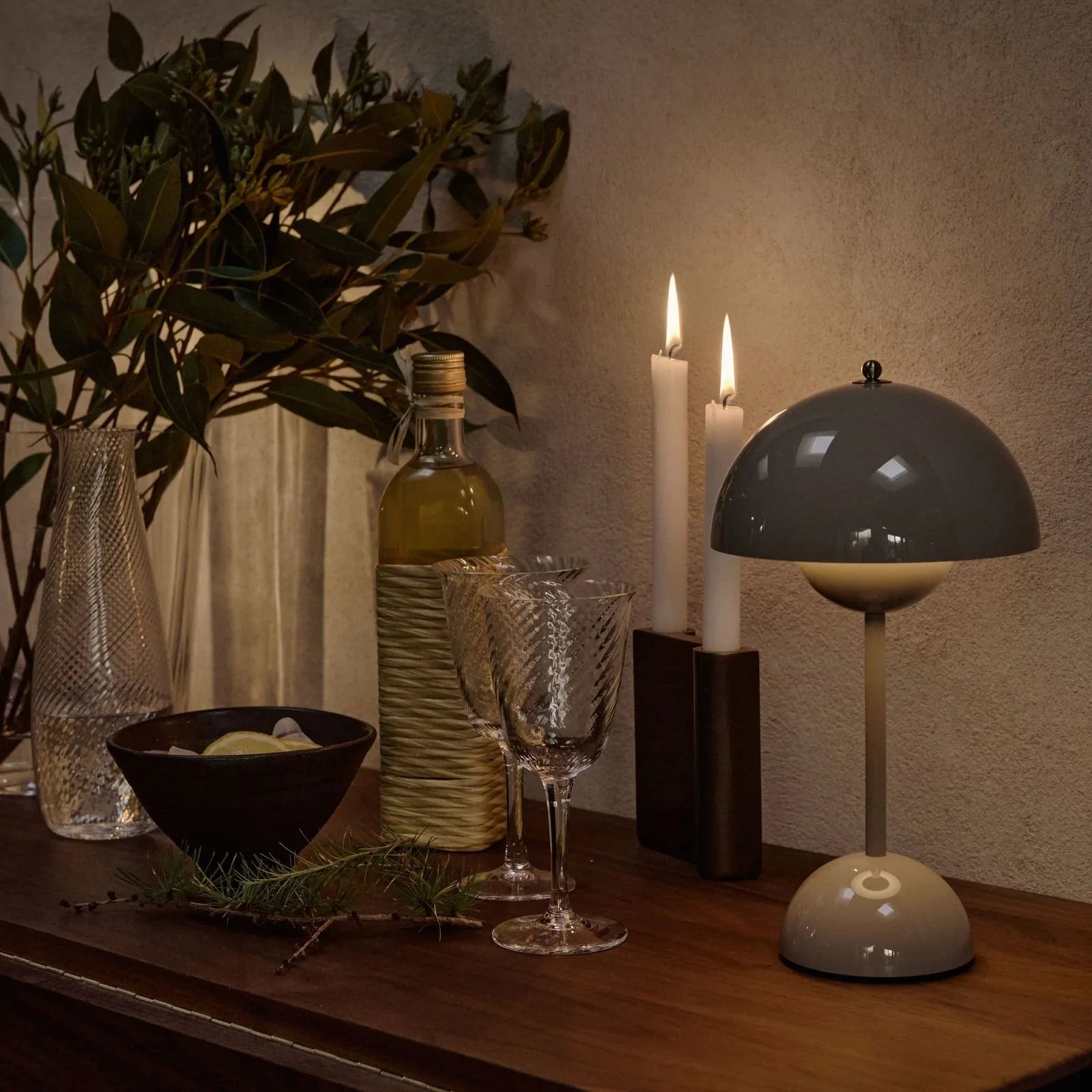 Modern dome table lamp with warm glow, styled with candles, wine glasses, and greenery for cozy ambiance