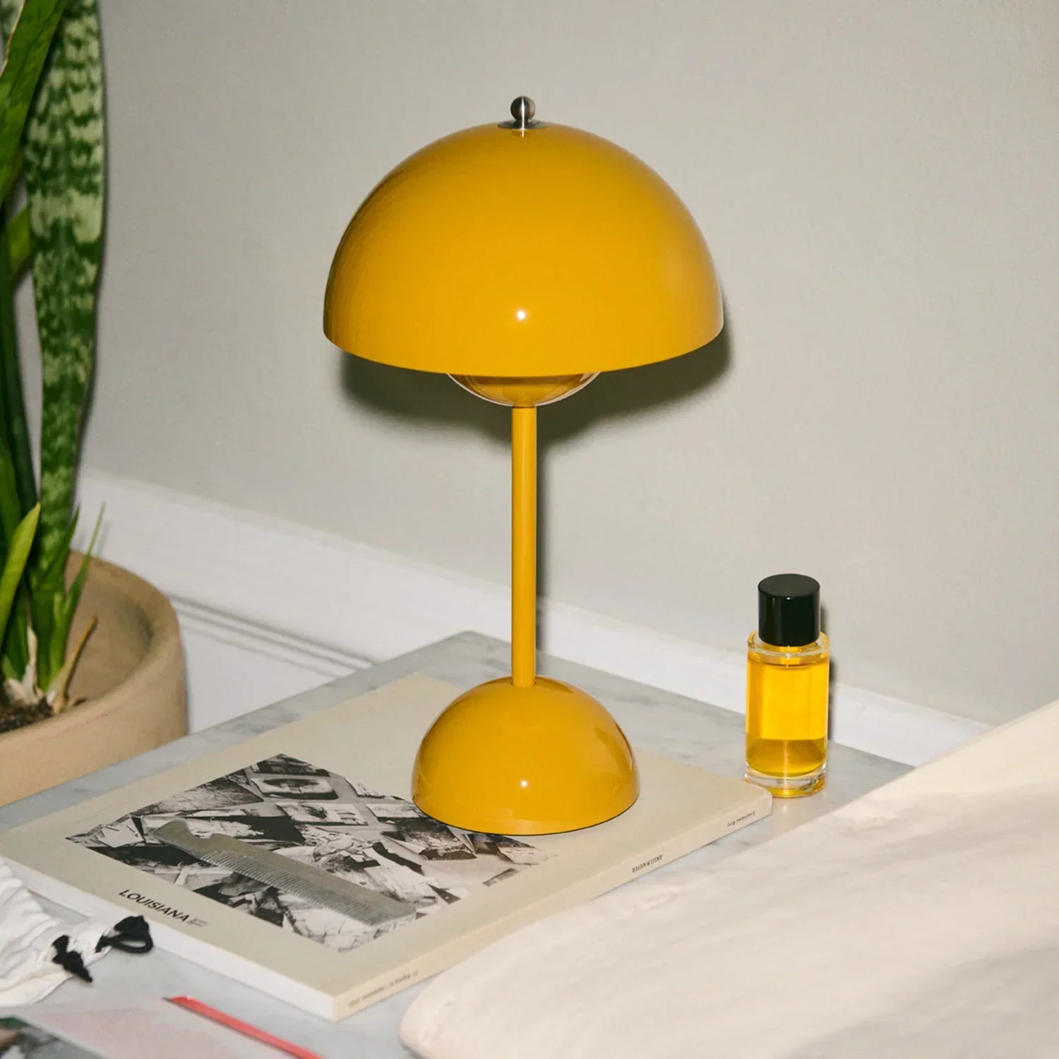 Vibrant yellow dome table lamp on marble nightstand with plant and perfume, groovy bedroom lighting