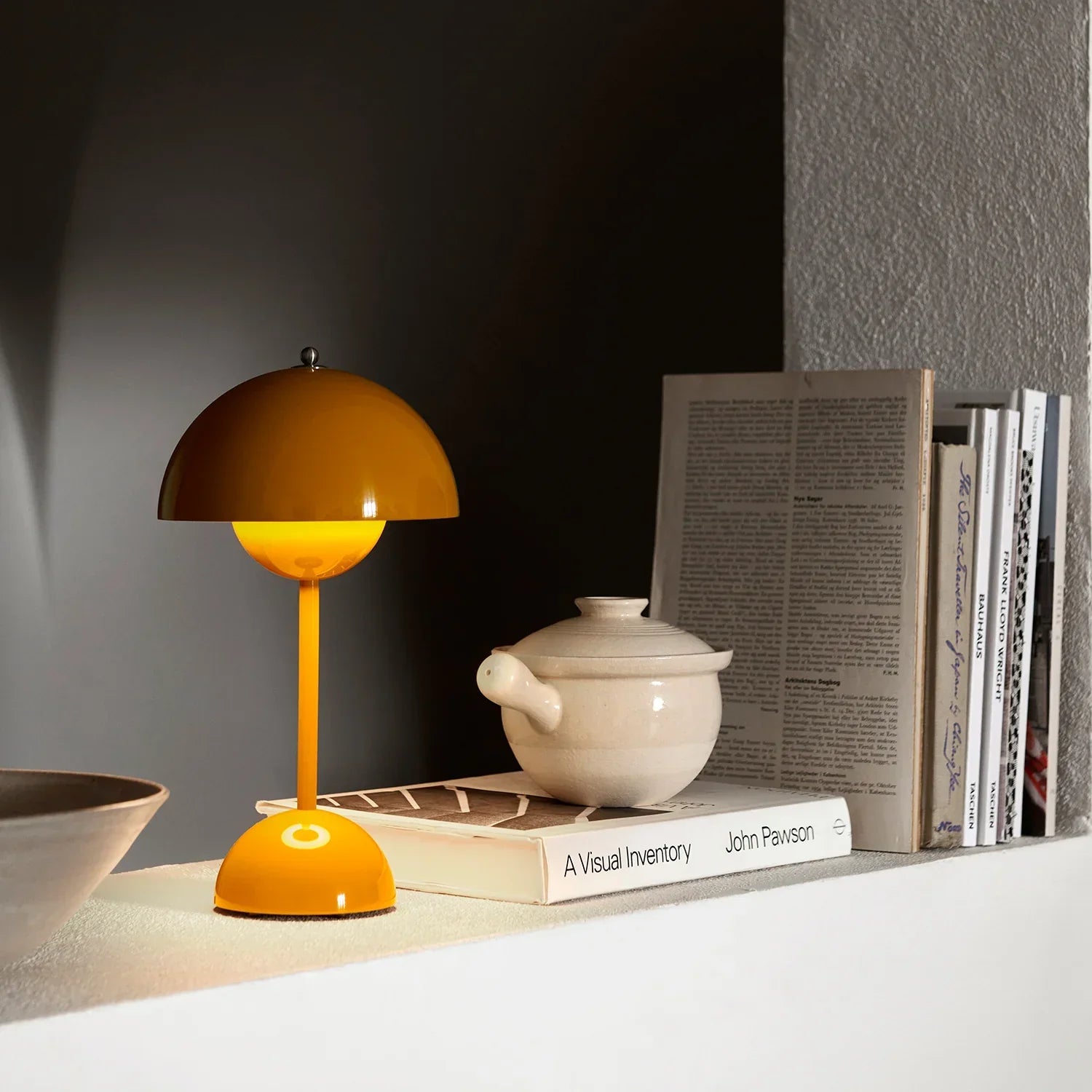 Vibrant orange mushroom-style table lamp on shelf with books and ceramic pot
